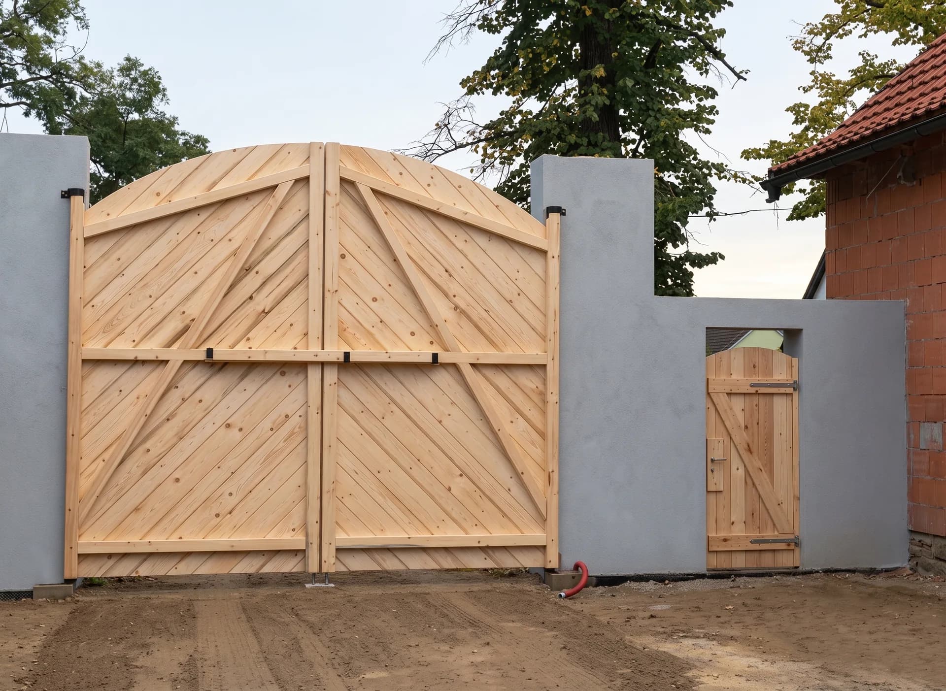 Vrata z čerstvého dřeva s diagonálním kladením a samostatnými vrátky vedle hlavního vjezdu.
