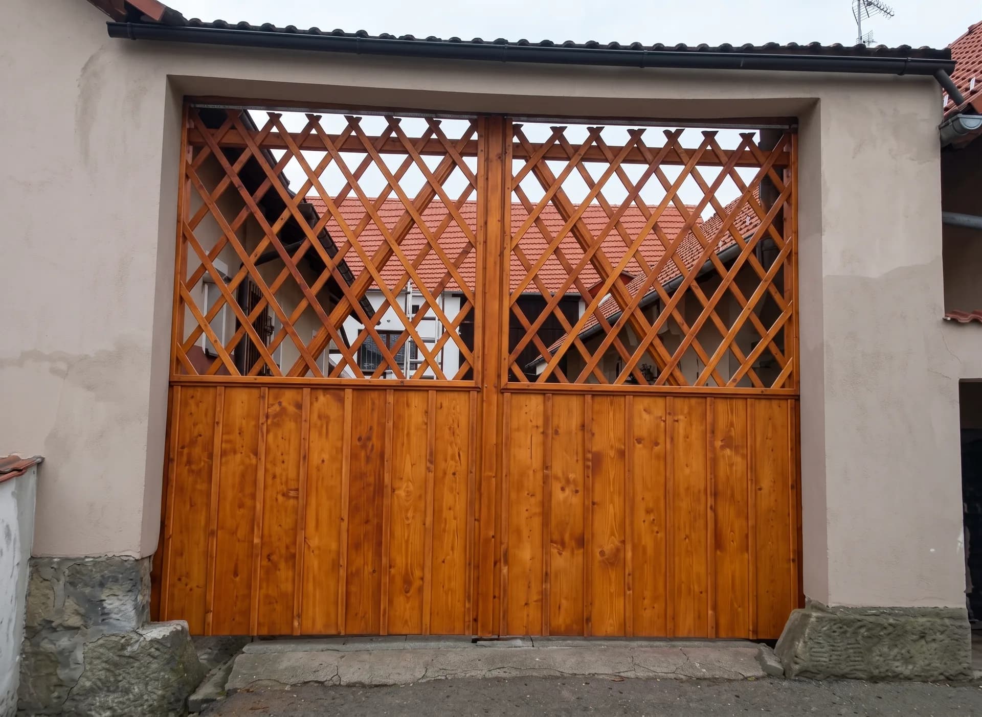 Vrata do průjezdu s horní diagonální mříží a spodními palubkami, v medovém odstínu.